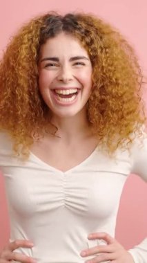 Saf mutluluk saçan neşeli kızıl saçlı kadın, yumuşak pembe stüdyo arkaplanına karşı bulaşıcı bir neşeyle kıkırdıyor, parlak gülümseme ve kaygısız tavırlarla gerçek olumlu duygular ifade ediyor.