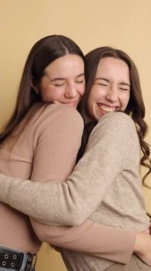 İki arkadaş sıcak bir kucaklaşmayı paylaşıyor ve bej bir arkaplanda neşeyle gülüyor, bir arkadaşlık ve mutluluk anı yakalıyorlar.