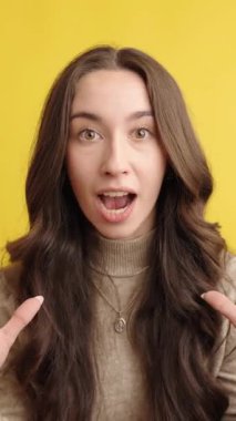 Heyecanlı bir kadın, şaşkın, heyecanlı ve meraklı bir ifadeyle canlı sarı bir arkaplan karşısında çeşitli yüz ifadeleri sergiliyor. Bir dizi duyguyu dinamik bir şekilde yakalar