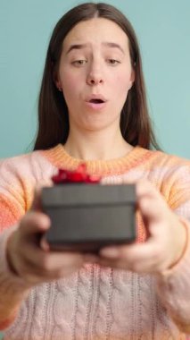 Sürpriz bir hediye kutusu alan ve üzerine titreyen mutlu bir kadın, deniz mavisi arka planında çeşitli neşeli ifadeler sergiliyor.