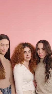 Kadınlar bir dizi neşeli ve abartılı yüz ifadeleri sergilerken, aynı zamanda basit bir pembe arkaplana karşı poz veriyorlar, arkadaşlık ve eğlenceyi aktarıyorlar.