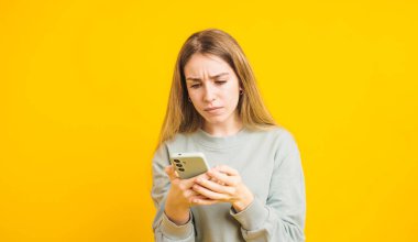 Genç bir kadın cep telefonu kullanırken kaşlarını çatıyor. Endişelerini dile getiriyor ve parlak sarı bir arka plan için endişeleniyor.