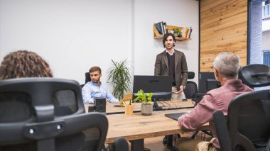 Yaratıcı ofis ortamında bilgisayar masalarının başında duran kendine güvenen işadamı, ortak ve yenilikçi çalışma alanlarında tartışmalara öncülük ediyor ve fikirleri paylaşıyor.