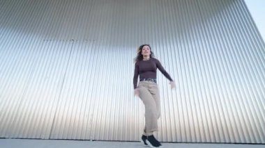 Enerjik kadın dansçı kıvrımlı metal duvar arka planına karşı çağdaş bir şehir dansı gösterisi yapıyor.