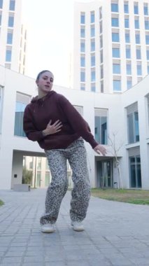 Dinamik sokak dansçısı modern şehir binasının önünde sanatsal ifade ile enerjik hip hop hareketleri sergiliyor, serbest dans becerileri sergiliyor ve çağdaş tarz sergiliyor.