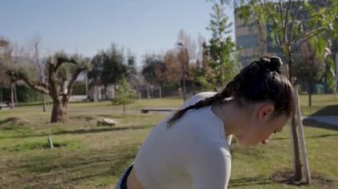 Dinamik esneme ve ısınma egzersizleri yapan bayan sporcu yaz mevsimi boyunca yeşil manzarayla çevrili güneşli parkta antrenman yaparken spor giyer.
