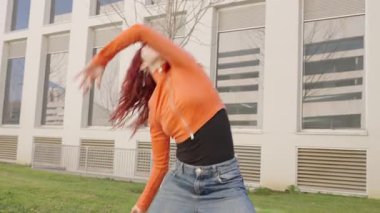 Kızıl saçlı sanatçı beyaz mimari yapının yanında dinamik kent dans koreografisi uyguluyor, yaratıcı hareketi ve sanatsal ifadeyi somutlaştırıyor