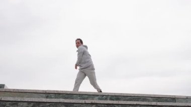 Genç erkek parkçı sporcu dinamik akrobatik yetenekler sergiliyor, fitness antrenmanı sırasında kentsel yapı çıkıntısında kesinlikle atlıyor ve takla atıyor.