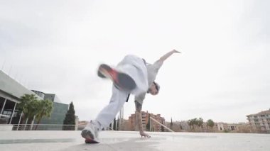 Breakdansçı akrobatik yeteneklerle hareketler sergiliyor şehir meydanında açık gökyüzünün altında sokak dansı enerjisi sergiliyor.