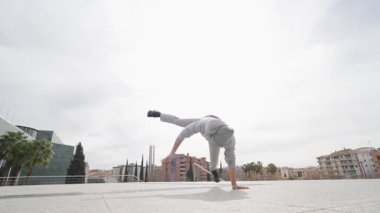 Breakdance sanatçısı şehir meydanı ortamında enerjik sokak dansı sırasında dinamik akrobatik hareketler yapıyor.