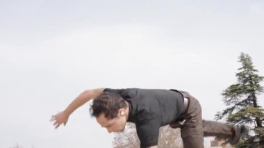 Breakdansçı yüksek enerjili break dans hareketleri yapıyor, dinamik akrobatik yetenekler sergiliyor ve güneşli park ortamında sokak dansı yapıyor.