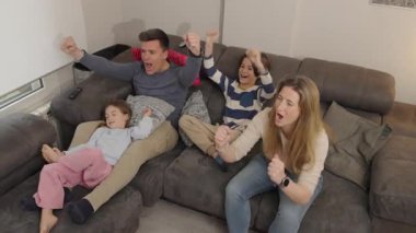 Mutlu bir aile rahat bir koltukta eğleniyor, favori takımları için tezahürat yapıyor ve birbirlerini gıdıklıyorlar.