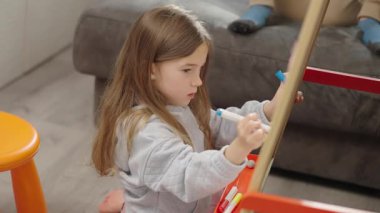 Kız beyaz tahtaya resim çiziyor, yaratıcılığı keşfediyor ve ev ortamında oyun oynayarak öğreniyor.