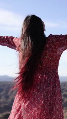 Uzun saçlı, özgürlüğünü ifade eden kolları açık ve dans eden bir kadın güzel bir doğal ortamda dans eder.