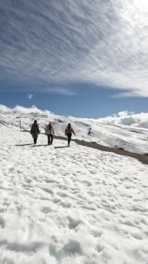 Dağlar ve dinamik gökyüzü ile çevrili, karla kaplı bir dağda yürüyen bir grup maceraperest, keşif ve takım çalışması öneriyor.