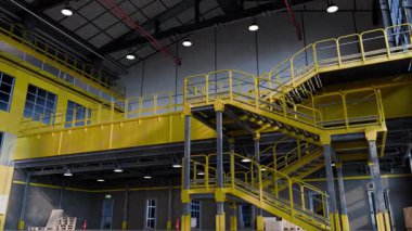 Güneş ışığı sarı metal merdivenleri aydınlatıyor ve büyük boş bir sanayi deposunun içinde yürüme yollarını aydınlatıyor.