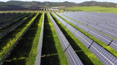 Sıralar halindeki güneş panelleri güneş ışığını yakalar, uzaktaki rüzgar türbinleriyle tamamlanmış bir alanda temiz enerji üretirler.