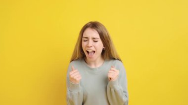 Coşkulu genç kadın başarıyı kutluyor, mutluluk ve heyecanı canlı sarı bir arkaplan önünde neşeli yüz ifadeleriyle ifade ediyor.