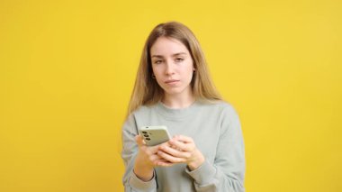 Genç bir kadın hüzün, can sıkıntısı ve hayal kırıklığı gibi olumsuz duygular sergiliyor. Elinde canlı sarı bir arkaplana karşı akıllı bir telefon tutuyor.