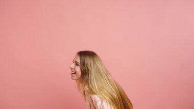 Genç kadın, neşeli duygular sergiliyor, kahkahadan sıcak bir gülümsemeye, pembe bir arka plana karşı, gerçek mutluluk ve neşe hislerini yakalıyor.