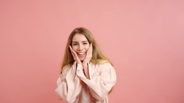 Genç bir kadın, pembe bir arka plana karşı çeşitli neşeli ve sürpriz ifadeler sergiliyor. Neşeli bir sekansta bir dizi duyguyu somutlaştırıyor.