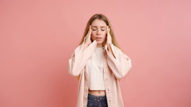 Baş ağrısı çeken genç bir kadının stüdyo fotoğrafı. Şakaklarına ve alnına elleriyle dokunuyor. Rahatsızlık ve acı gösteriyor.