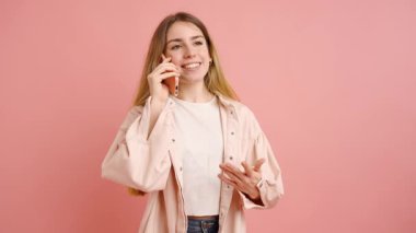 Gündelik giysiler giyen sarışın kadın çeşitli telefon konuşmalarına katılıyor, canlı pembe bir fon karşısında çeşitli duygu ve jestler sergiliyor.