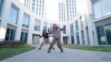 İki kadın dansçı modern bir binanın önünde koreografik dans gösterisi yapıyorlar.