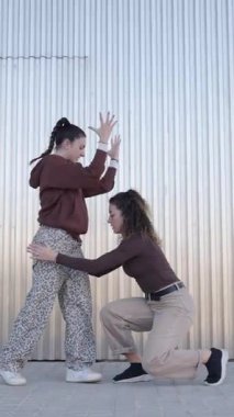 İki genç kadın, muhtemelen profesyonel dansçılar, kıvrılmış metal bir duvara karşı kentsel dans yeteneklerini sergiliyorlar.