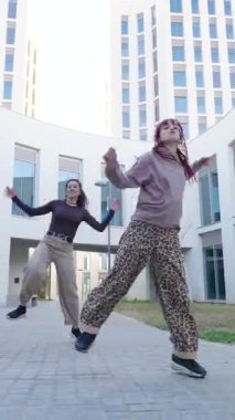 İki kadın dansçı koreografili bir açık hava gösterisi sergiliyor, çağdaş mimarinin arka planına karşı enerjik hareketler sergiliyorlar.