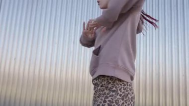 Kızıl saçlı dansçı gündelik giysiler giyip metal bir duvara karşı modern bir dans koreografisi sergiliyor.