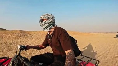 Çöl manzarası sonsuz ufukla birleşirken turistler dörtlü bisikletteki engebeli arazide geziniyor, kumlu çöllerde adrenalin dolu maceralar yaşıyor.