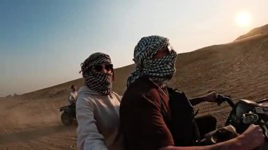 Çöl batımı dörtlü bisiklet macerası: turistler altın kum tepeciklerini aşarak, sıcak, canlı akşam ışığı altında, off-road keşiflerinin özgürlüğünü ve heyecanını yaşıyorlar.