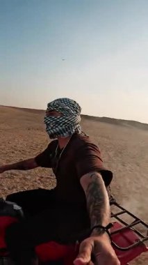Çöl maceracısı geleneksel keffiyeh giyerek kum tepelerinde dörtlü bisiklet sürüyor, özgürlüğü somutlaştırıyor ve yoğun güneş ışığı altında heyecan verici açık hava keşifleri yapıyor.