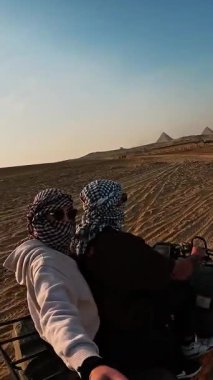 Maceraperest turistler ikonik giza piramitlerinin yakınındaki kumlu çöl arazisinde gezerler parlak mavi gökyüzü altında heyecan verici Mısır manzarası yaşarlar.