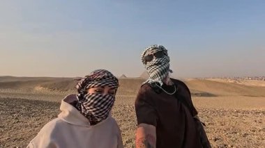 Keffiyeh giyen turistler Mısır 'daki Giza piramitlerinin yakınındaki çölde selfie çekiyorlar.