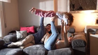 Mutlu bir aile, oturma odasındaki rahat bir kanepede yatarken kızlarını havaya kaldırıyor.
