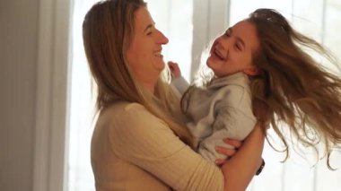 Sevgi dolu bir anne, genç kızıyla bağ kurar, gerçek neşe, kahkaha ve şefkat anlarını paylaşır, evin penceresinin yanında yumuşak doğal ışıkla kucaklaşır.