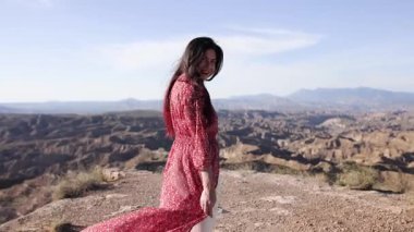 Geniş tabernalar ve çöl manzaraları arasında duran kırmızı elbiseli kadın model, Almerya 'da dağ arkaplanı ve dramatik gökyüzü ile manzaralı manzarayı inceliyor, İspanya