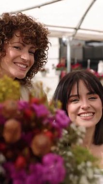 Çiçekçi ya da markette renkli bir buket çiçek tutan ve koklayan iki neşeli kadın. Dikey