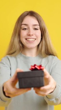 Kırmızı kurdeleli hediye kutusunu tutan kadın, gerçek mutluluğu yayıyor ve neşe dolu hediye verme ve alma anlarında içten şükranlarını sunuyor.