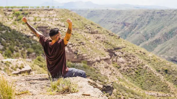 Bir kayanın üzerinde oturan turist, kutlamak için kollarını kaldırırken İspanya 'nın çarpıcı çöllerinde sırılsıklam oluyor.