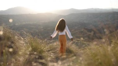 Enerjik bir neşeyle dans eden kadın, dramatik günbatımı anlarında altın renkli kanyon manzarasında sıçrayan, saf özgürlük ve vahşi doğa keşiflerini somutlaştıran kadın.
