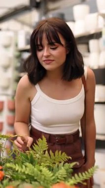 Bahçedeki çiçekleri seçerken çeşitli bitkilerin kokusundan hoşlanan genç bir kadın. Dikey