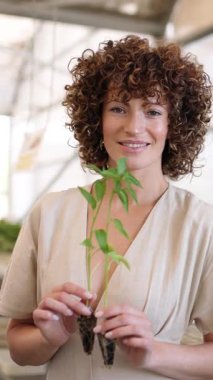 Hevesli bahçıvan sera ortamında taze bitki fidanları tutuyor, neşe ve besleyici doğayı ifade ediyor. Dikey