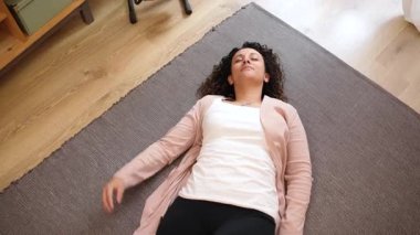 Huzurlu bir kadın rahat bir şekilde yumuşak halıda uzanıyor. Huzurlu bir evde dinlenirken yavaşça pozisyon değiştiriyor.