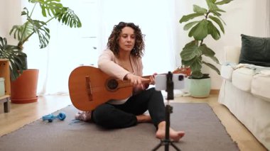 Ev tabanlı online müzik dersi sırasında akustik gitar çalan bayan müzisyen, dijital öğretim platformu aracılığıyla kişisel sanatsal ifadeleri yakalıyor
