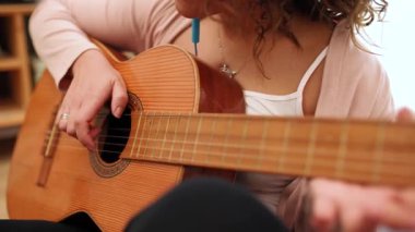 Kadın müzisyen gitar akorları çalışıyor, parmaklar fretboard üzerinde ustalıkla hareket ederken akustik enstrüman üzerinde melodik sesler yaratıyor.