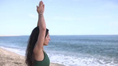 Yoga eğitmeni sakin bir plajda urdhva hastasana pozu vererek sağlığını ve farkındalığını arttırıyor.