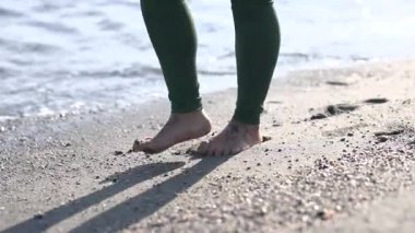 Çorap giyen bir kadın deniz kıyısında yalınayak yürümekten zevk alır, ıslak kumda ayak izleri bırakır.